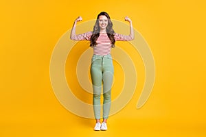 Full length body size photo of girl showing strong biceps with long hair smiling with hands isolated on vibrant yellow