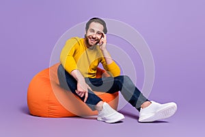 Full length body size photo guy sitting in beanbag smiling in casual outfit isolated pastel purple color background