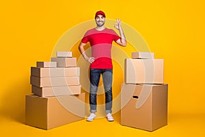 Full length body size photo happy courier with carton boxes showing okay gestured fingers isolated on vivid yellow color photo