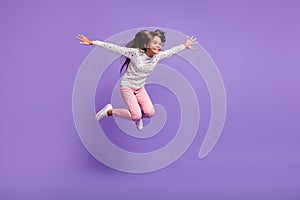 Full length body size photo little girl with long hair jumping high smiling happily isolated on bright violet color