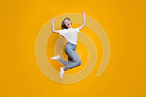 Full length body size photo of young girl fan jumping high gesturing like winner isolated on vibrant yellow color