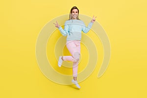 Full length body size view of attractive cheerful girl jumping showing v-sign isolated over bright yellow color