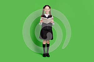 Full length body size view of attractive cheerful schoolgirl reading book isolated over bright green color background