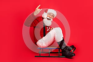 Full length body size view of nice comic cheerful Santa showing horn sign sleighing isolated over bright red color