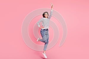 Full length body size view of pretty cheerful girl jumping showing v-sign good mood isolated over pink pastel color