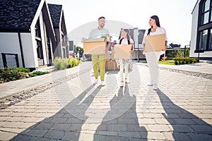 Full length body size view of three cheery family walking carrying packages cardboard belongings stuff to residence in