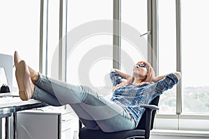 Full-length of businesswoman relaxing with feet up at desk in creative office