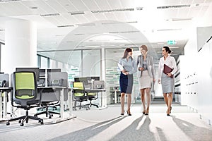 Full-length of businesswomen with file folders walking in office photo