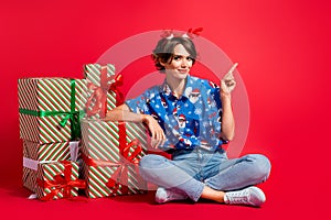 Full length cadre sit floor girl wear santa claus shirt print deer horns direct finger mockup stack gifts isolated on