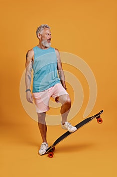 Full length of carefree senior man skateboarding while standing against orange background