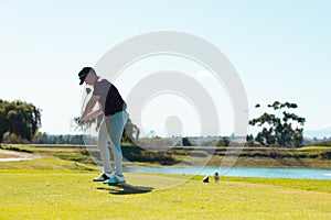 Full length of caucasian young man taking golf shot on grassy land at golf course against clear sky