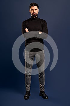 Full length of charming young man looking at camera and keeping arms crossed while standing against Pacific Blue background