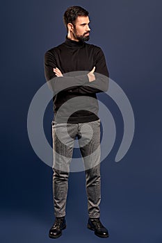 Full length of charming young man looking side and keeping arms crossed while standing against Pacific Blue background