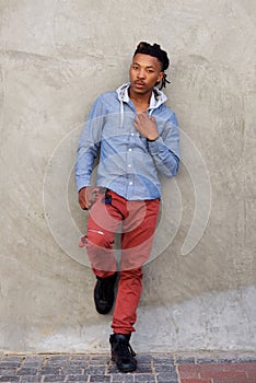 Full length cool african man with dreadlocks leaning against wall