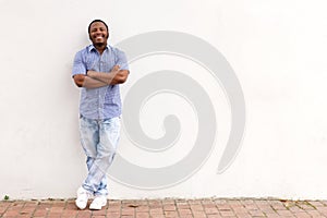 Full length cool young african man leaning against white wall and smiling