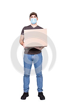 Full length delivery man holding a cardboard parcel box, wearing face mask as COVID-19 virus prevention measure, isolated on white