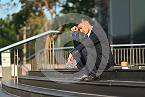 Full length of disappointed man sitting on stairs outside office building, lost job due financial crisis employee