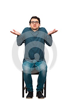 Full length of doubtful businessman, keeps hands outstretched, shrugging shoulders gesture, sitting on a chair isolated on white