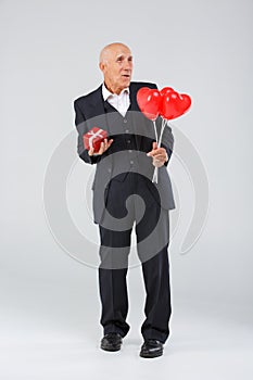 Full-length elderly man on a white background, in the studio, in a black smart suit with balls in his hand and a red