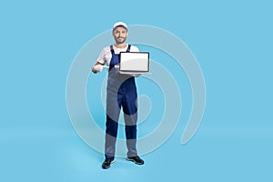 Full length expert worker man in uniform pointing at laptop with mock up blank display, showing advertise