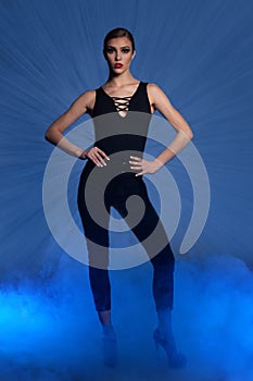 Full length fashon photo of a woman standing over dark background with smoke around her