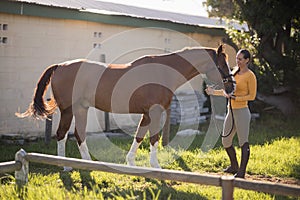 Full length of female jockey with horse standing on field at barn