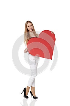 Full length girl holding up a red cardboard heart, ioslated on w