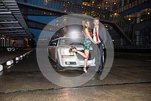 Full length of glamorous young couple standing in front of limousine on street at night