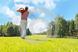 Full length of golf player playing golf on sunny day. Professional male golfer taking shot on golf course.