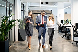 Full length of group of happy young business people walking the corridor in office together