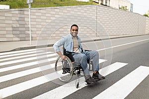 Full length of handicapped black man in wheelchair crossing street, using crosswalk outdoors