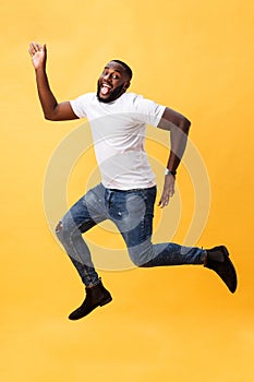 Full length of handsome young black man jumping against yellow background.