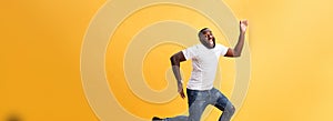 Full length of handsome young black man jumping against yellow background.