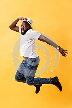 Full length of handsome young black man jumping against yellow background.