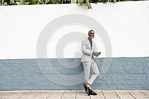 Full length happy  businessman leaning against wall by street with mobile phone