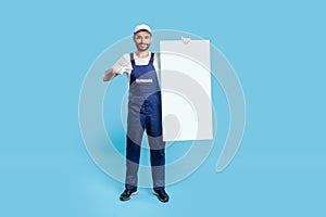 Full length of happy labourer man in uniform and protective gloves pointing at vertical poster template