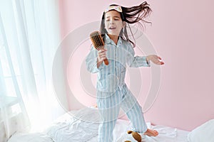 Full-length of a happy little girl in pajama jumping on the bed holding a hair brush like microphone singing imitates herself a