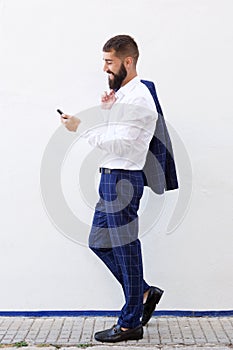 Full length happy man walking with mobile phone by white wall