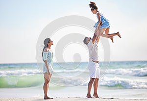 Full length of a happy mixed race family enjoying family time together at the beach. Loving father lifting his daughter