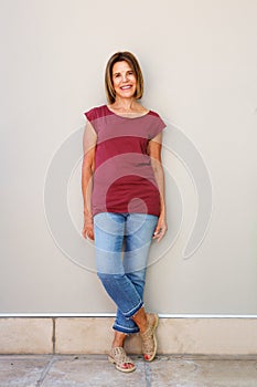 Full length happy older woman leaning against wall