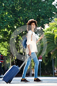 Full length happy traveler walking with suitcase and mobile phone in park