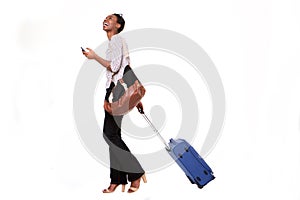 Full length happy young african american woman walking with luggage and smart phone on isolated white background