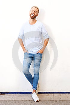 Full length happy young man leaning against white wall