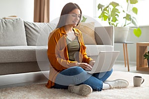 Full length of happy young woman sitting cross legged on floor with laptop pc, working or studying online at home