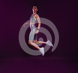 Full length of a healthy woman in silver sportswear jumping in the air