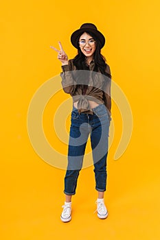 Full length image of asian woman smiling and gesturing peace fingers