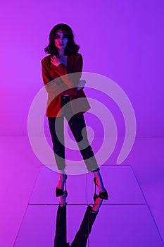 Full length image of an attractive brunette model posing in red suit ang black jeans in mixed neon light.