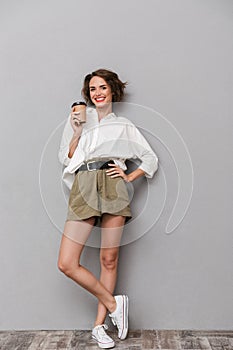 Full length image of attractive woman 20s smiling and holding ta