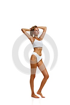 Full-length image of attractive young girl with beautiful, fit, slim body standing in underwear against white studio