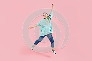 Happy brunette woman with canecalons in oversize hoodie jumping and looking at the camera over pink background